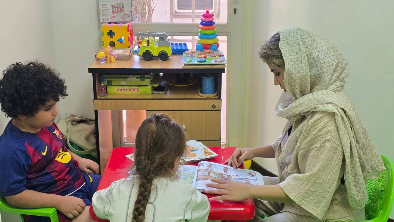 درمانگر و دو کودک در حال کتاب‌خوانی